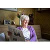 Senior woman reading morning newspaper, sitting in her favorite chair in her living room, looking happy