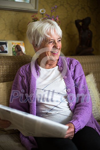 Senior woman reading morning newspaper, sitting in her favorite chair in her living room, looking happy Senior woman reading morning newspaper, sitting in her favorite chair in her living room, looking happy