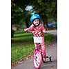 Cute smiling little girl with bicycle and helmet on road in the park