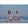 young couple practicing yoga at sunset in modern home terace with ocean and sunset in background