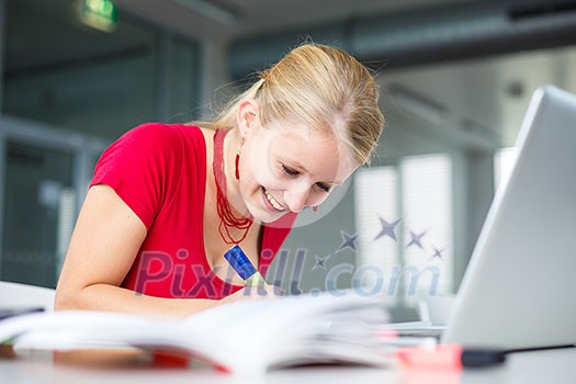 In the library - pretty, female student with books, papers and laptop computer working in a high school library (color toned image)