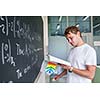 Handsome college student solving a math problem during math class in front of the blackboard/chalkboard (color toned image)