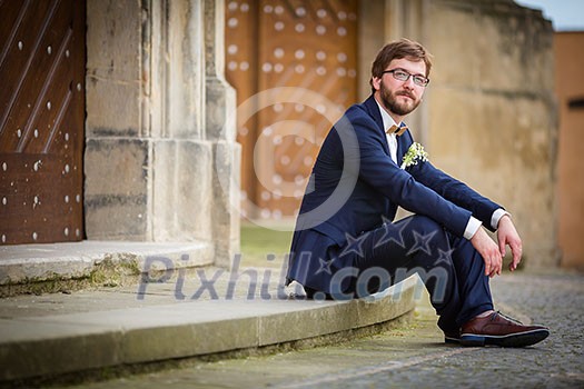 Handsome groom on his wedding day waiting for his bride in front of a church
