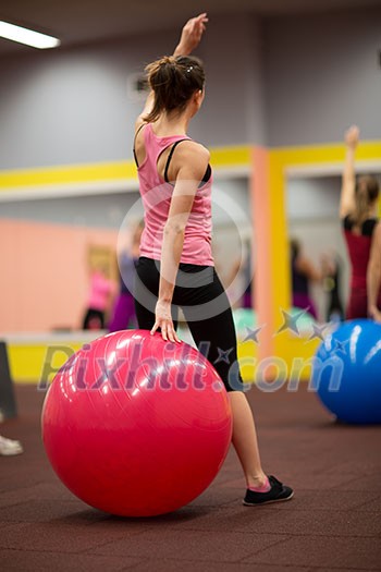 Group people in a pilates class at the gym - young woman with gymball at fitness training (shallow DOF, color toned image)