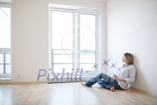 Just moved in: beautiful young woman finally sitting down and relaxing -  having a drink in her brand new modern apartment