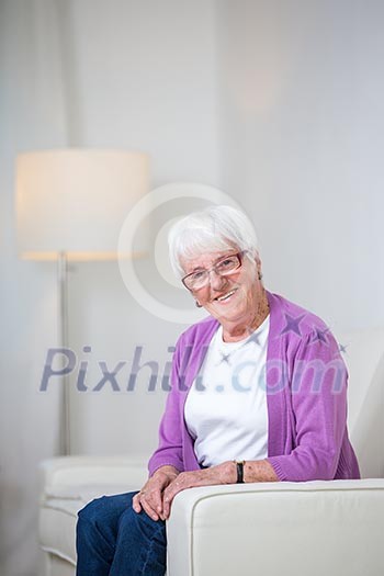 Portrait of a senior woman at home - Looking happy, looking at the camera, smiling while sitting on the sofa in her living room Portrait of a senior woman at home - Looking happy, looking at the camera, smiling while sitting on the sofa in her living room
