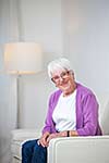 Portrait of a senior woman at home - Looking happy, looking at the camera, smiling while sitting on the sofa in her living room