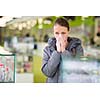 Young woman blowing her nose while in a modern pharmacy, choosing pills to help her with the flu/cold (shallow DOF; color toned image)