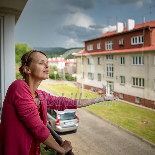 Pretty, young woman checking wether it is raining already from the balcony of her appartment