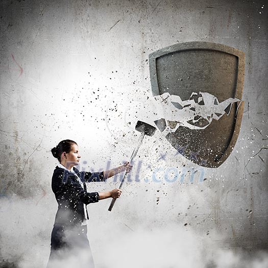 Young businesswoman crashing stone shield with hammer Young businesswoman crashing stone shield with hammer