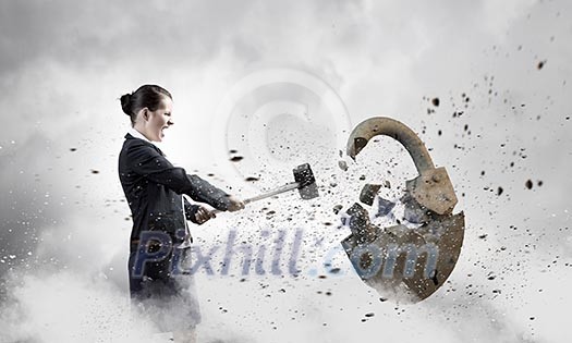 Young angry businesswoman crashing stone lock with hammer Young angry businesswoman crashing stone lock with hammer