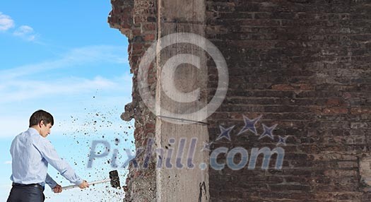 Young determined businessman breaking wall with hammer