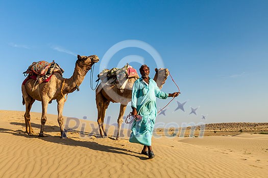 Rajasthan travel background - Indian cameleer (camel driver) with camels in dunes of Thar desert. Jaisalmer, Rajasthan, India