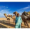 Rajasthan travel background - Indian man cameleer (camel driver) portrait with camels in dunes of Thar desert. Jaisalmer, Rajasthan, India