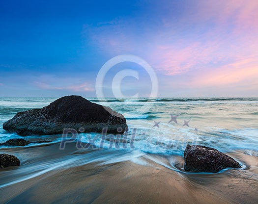 Tropical beach vacation background - waves and rocks on beach of sunset