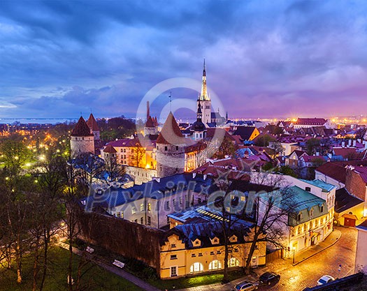 Aerial view of Tallinn Medieval Old Town with St. Olaf's Church and Tallinn City Wall illuminated in evening with dramatic cloudscape, Estonia Aerial view of Tallinn Medieval Old Town with St. Olaf's Church and Tallinn City Wall illuminated in evening with dramatic cloudscape, Estonia