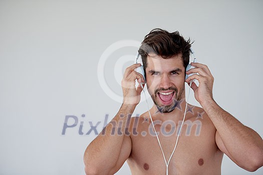 handsome young man listening music on headphones at modern home over  white wall and standing on hands