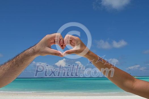 romantic couple make heart shape symbol of love with arms on sunny tropical beach and sea in background