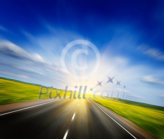 Travel concept background - motion blurred road in blooming spring meadow on sunset with blue sky
