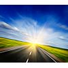 Travel concept background - motion blurred road in blooming spring meadow on sunset with blue sky