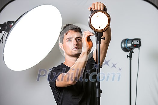 Young, pro photographer setting lights in his well equiped studio before a photo shoot (color toned image; shallow DOF)