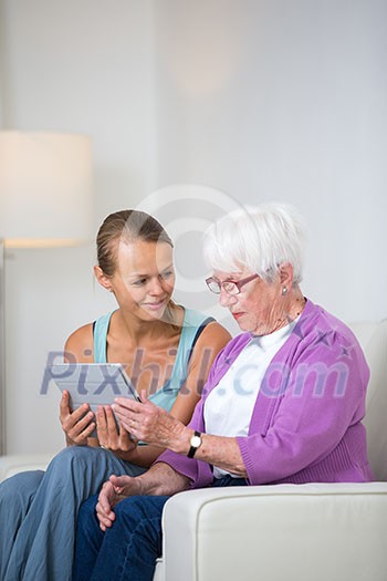 Grandmother with her grand-daughter sitting on a sofa, using a tablet computer, learning how to use technology