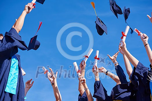 high school students graduates tossing up hats over blue sky.