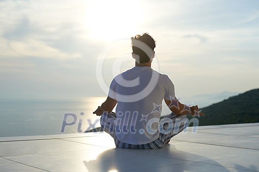 handsome young man practicing yoga on in modern home terace with ocean and sunset in background handsome young man practicing yoga on in modern home terace with ocean and sunset in background