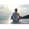 handsome young man practicing yoga on in modern home terace with ocean and sunset in background