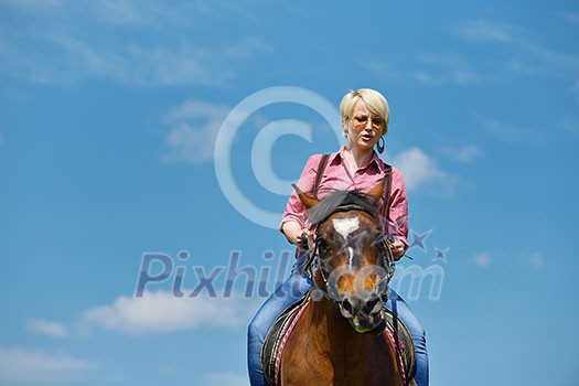 happy woman in sunglasses sitting on horse farm animal outdoors with blue sky in background