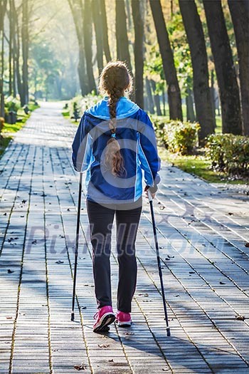 Nordic walking adventure and exercising concept - woman hiking withnordic walking poles in park