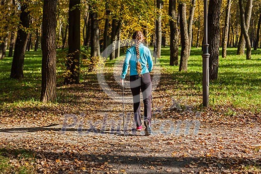 Nordic walking adventure and exercising concept - woman hiking withnordic walking poles in park