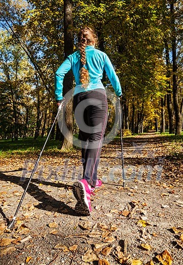 Nordic walking adventure and exercising concept - woman hiking withnordic walking poles in park