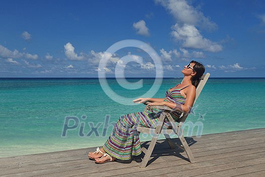 Beautiful young woman in bikini lying on a deckchair with a drink by the sea