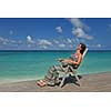 Beautiful young woman in bikini lying on a deckchair with a drink by the sea