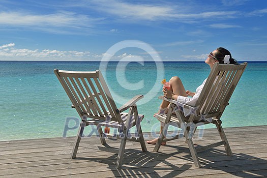 Beautiful young woman in bikini lying on a deckchair with a drink by the sea Beautiful young woman in bikini lying on a deckchair with a drink by the sea