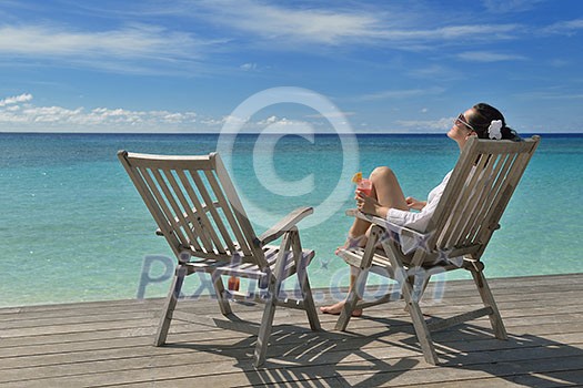 Beautiful young woman in bikini lying on a deckchair with a drink by the sea