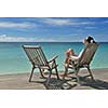 Beautiful young woman in bikini lying on a deckchair with a drink by the sea