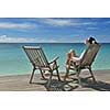 Beautiful young woman in bikini lying on a deckchair with a drink by the sea