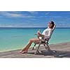 Beautiful young woman in bikini lying on a deckchair with a drink by the sea