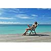 Beautiful young woman in bikini lying on a deckchair with a drink by the sea