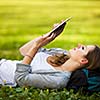 Young woman using her tablet computer while relaxing outdoors in a park on a lovely spring day