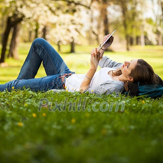 Young woman using her tablet computer while relaxing outdoors in a park on a lovely spring day Young woman using her tablet computer while relaxing outdoors in a park on a lovely spring day