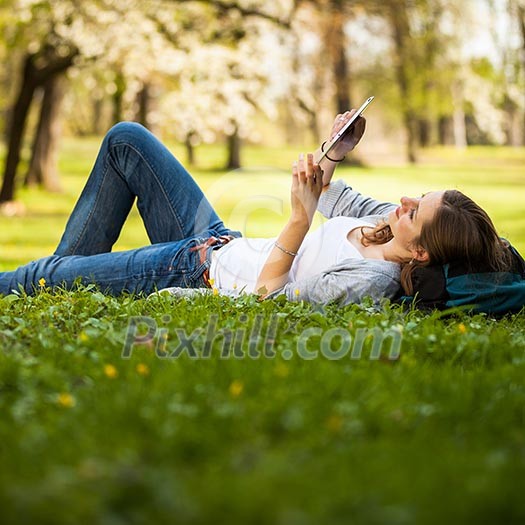 Young woman using her tablet computer while relaxing outdoors in a park on a lovely spring day