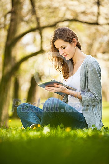 Young woman using her tablet computer while relaxing outdoors in a park on a lovely spring day