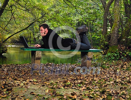 one young businessman working on laptop outdoor with green nature in backgroundone young businessman working on laptop outdoor with green nature in background