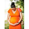 beautiful young happy pregnant woman outdoor in bright nature in orange dress