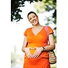 beautiful young happy pregnant woman outdoor in bright nature in orange dress