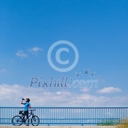 Background for poster or advertisment pertaining to cycling/sport/outdoor activities - female cyclist during a halt on a bridge against blue sky (color toned image) Background for poster or advertisment pertaining to cycling/sport/outdoor activities - female cyclist during a halt on a bridge against blue sky (color toned image)