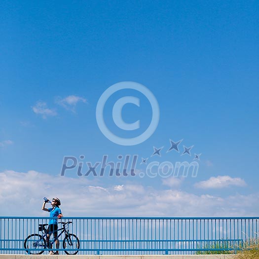 Background for poster or advertisment pertaining to cycling/sport/outdoor activities - female cyclist during a halt on a bridge against blue sky (color toned image)